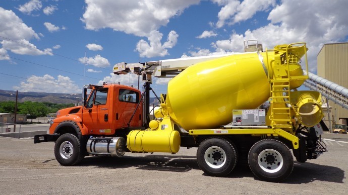 A yellow cement mixer is parked in front of a building.