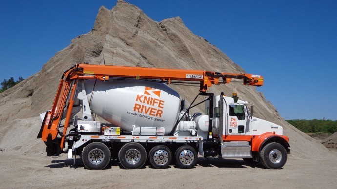 A large truck with a concrete mixer in front of a mountain.