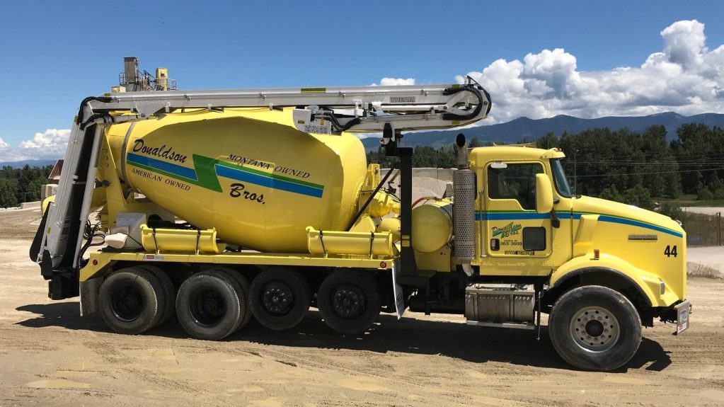 A yellow cement mixer is parked in a dirt lot.