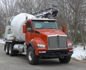 An orange and white cement truck driving down a snowy road.