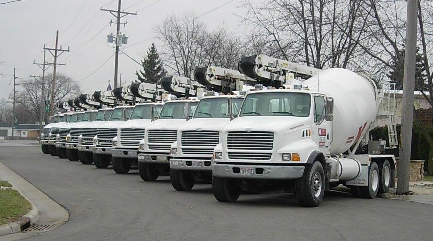 A row of white cement trucks parked on a street.
