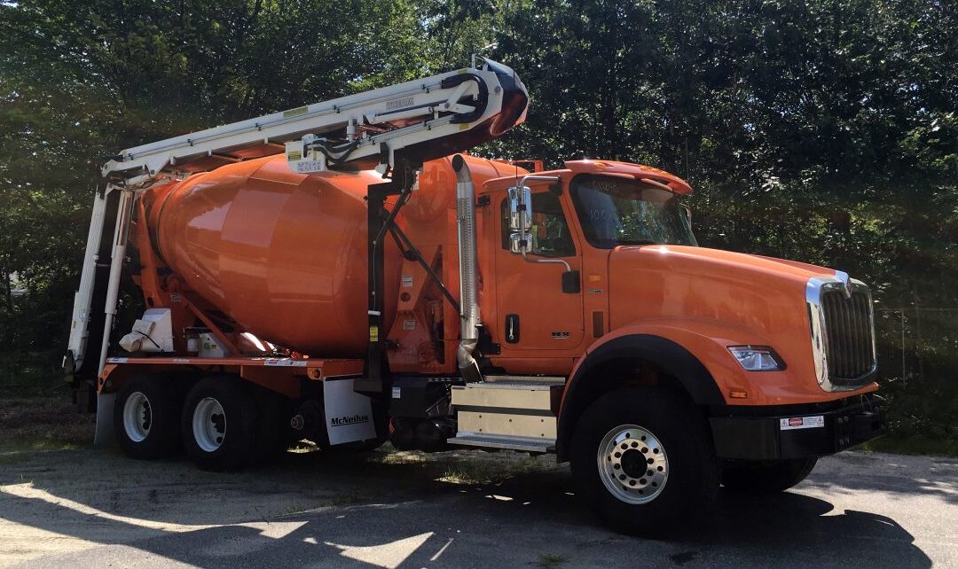 An orange cement mixer truck is parked in a parking lot.