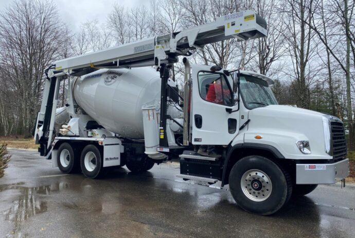 A white cement mixer truck is parked on the side of the road.