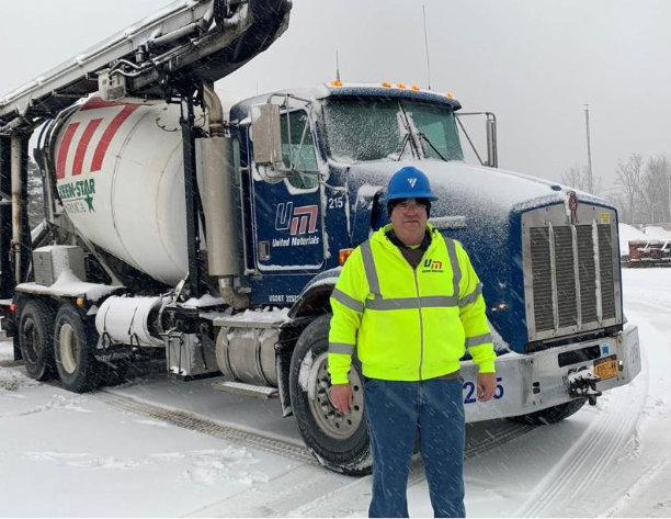 Ready-mix truck driver in a safety vest beside his mixer truck in the snow